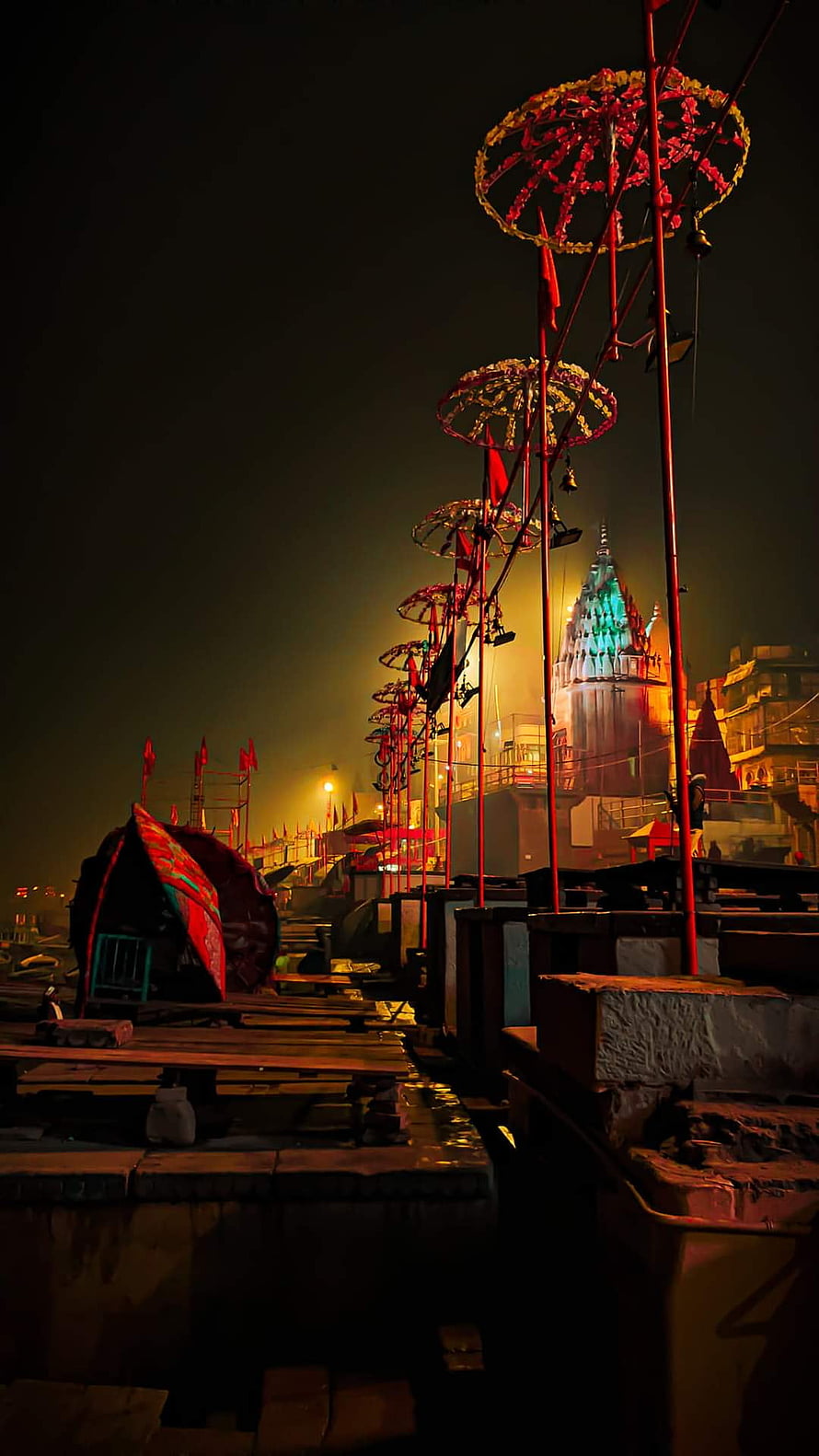 Varanasi Ghat at Night with Illuminated Temple and Decorated Poles HD phone wallpaper