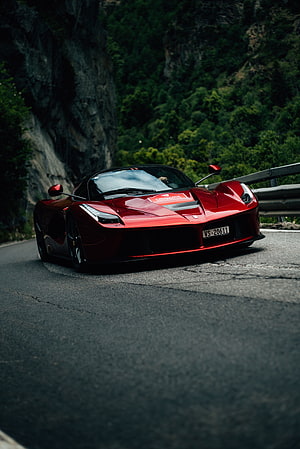 Red Ferrari LaFerrari driving on a winding mountain road with lush green forest background HD phone wallpaper