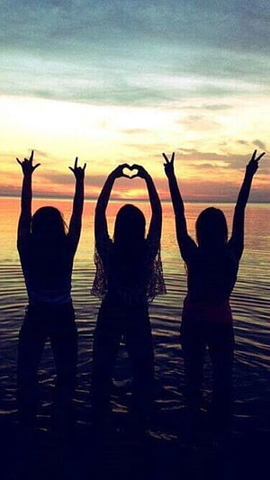Three Silhouetted Friends Making Hand Gestures Against a Sunset Ocean View HD phone wallpaper