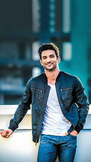 Sushant Singh Rajput smiling in a black leather jacket and blue jeans against a blurred urban background HD phone wallpaper