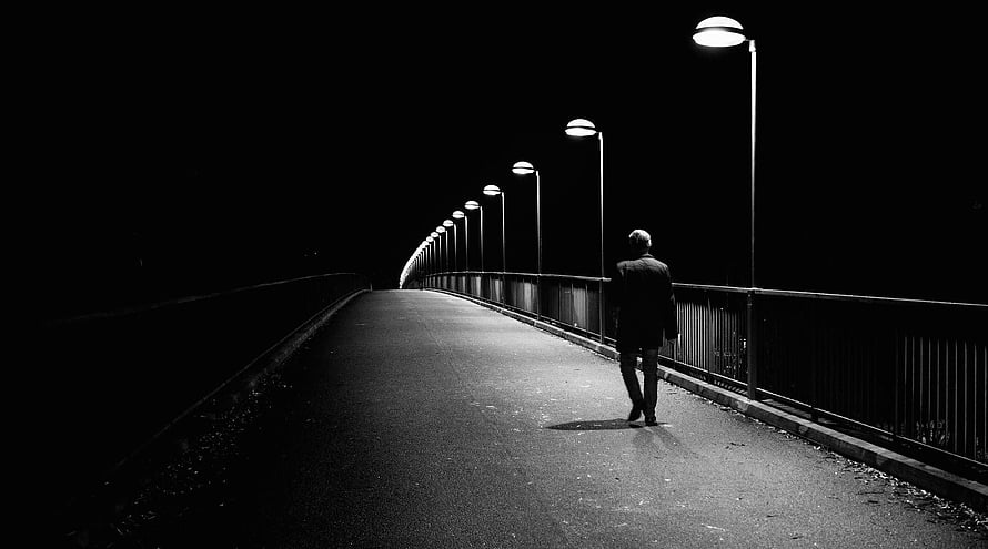 Solitary figure walking along a curved bridge at night under a row of street lamps in black and white HD wallpaper