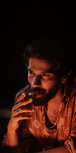 Dramatic portrait of a bearded man smoking a cigarette in warm orange lighting, Dulquer Salmaan, jaw, kurup HD phone wallpaper